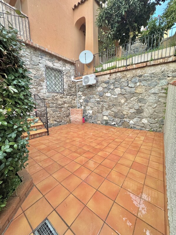 A courtyard with terracotta tiles, a stone wall, a satellite dish, and a small brick structure.