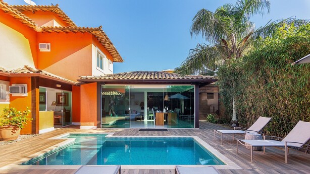 A swimming pool with lounge chairs, a wooden deck, and a glass-enclosed patio area. - Bz70 Casa Piscina 650m da Rua das Pedras (Buzios)