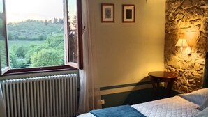 Ein Schlafzimmer mit großem Fenster, einer Steinwand, einem Bett mit Steppdecke, einem Nachttisch und einer Lampe.