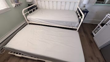 A twin bed with a white mattress in a room with light green walls, a wooden floor, and a small bedside table with a lamp.
