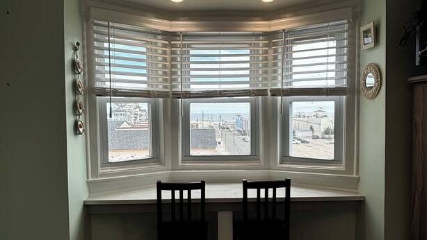 A bay window with three panes, a table, and two chairs in a room with wooden flooring and light green walls.