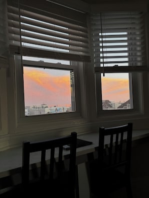 Una habitación con dos ventanas con persianas, una mesa y dos sillas.