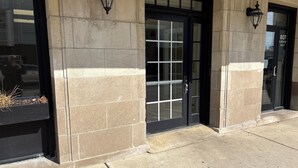 A building entrance with a black door, stone walls, and two black wall-mounted lanterns.