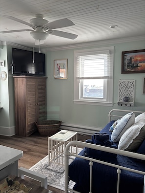 Un dormitorio con cama, televisión, ventilador de techo y ventana con persianas.
