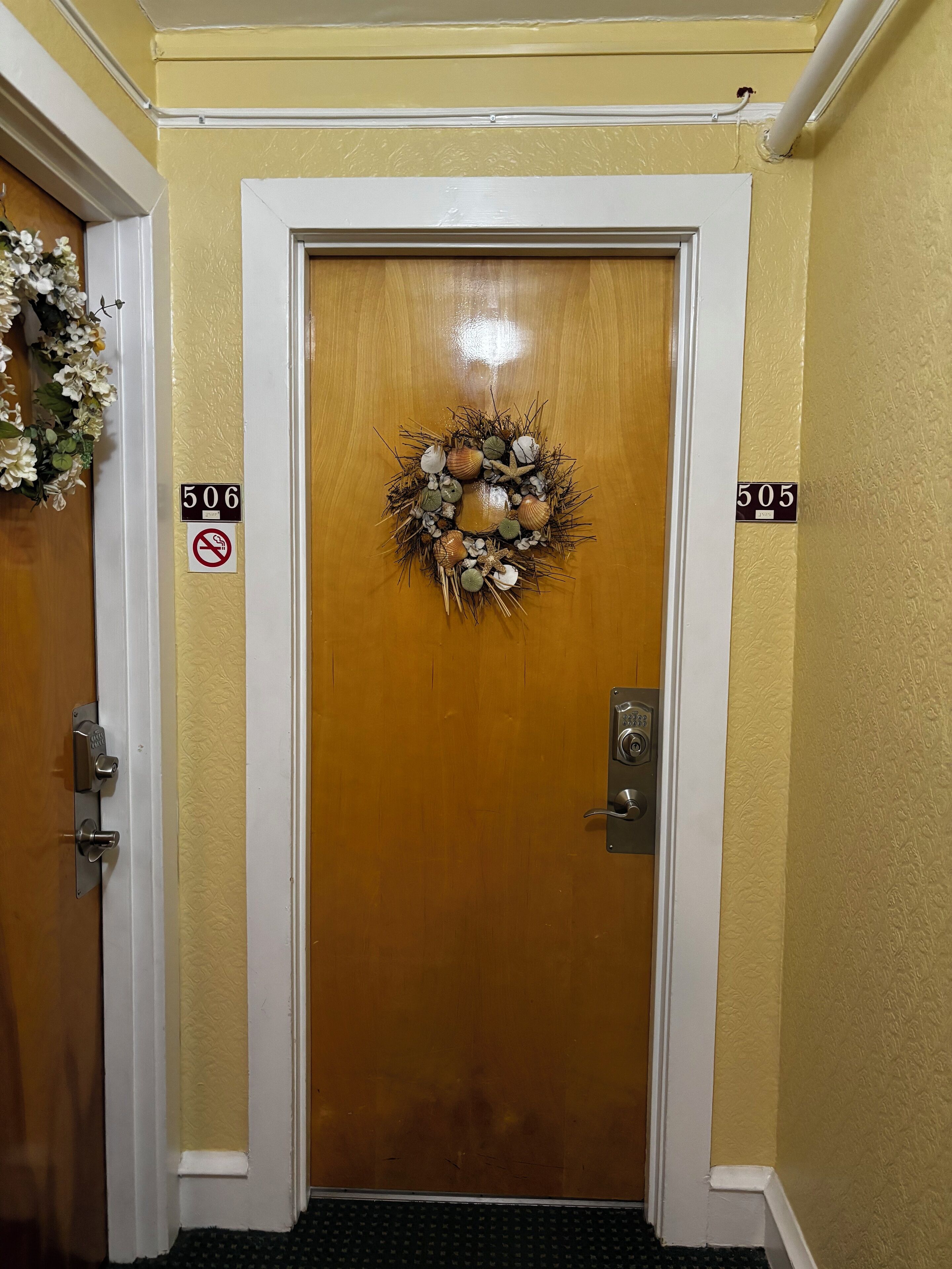 A wooden door with a wreath, numbers 506 and 505 on the walls, and a doormat.