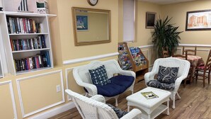 A room with wicker furniture, a bookshelf, a mirror, and a clock on the wall.