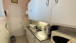 Uma cozinha compacta com armários brancos, pia, micro-ondas e geladeira.