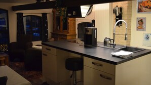 Una cocina con mostrador negro, cafetera, lavamanos y un taburete de bar.