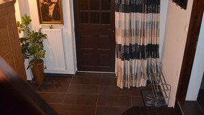 Un pasillo con una puerta de madera, un radiador, una planta en maceta y un zapatero metálico.