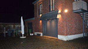 Un edificio de ladrillo con puerta de garaje, un espacio cubierto al aire libre y una sombrilla blanca.