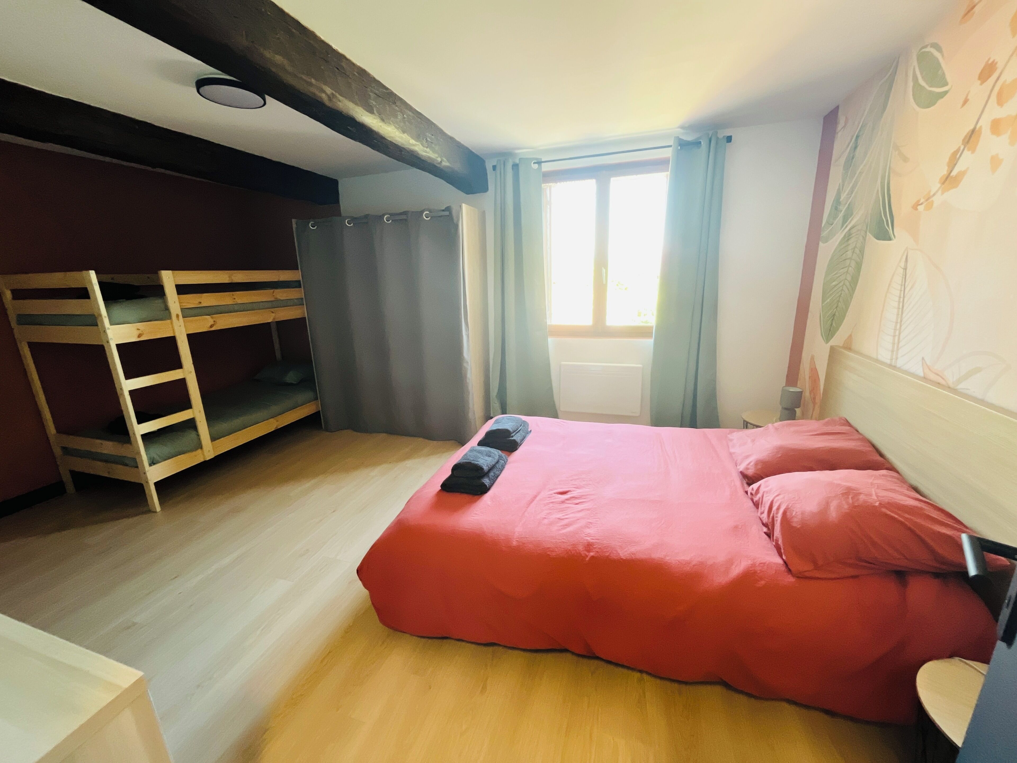 A room with a bunk bed, a single bed with red bedding, a window with curtains, and a wall with a leaf pattern.