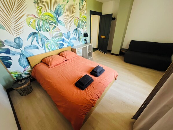 A room with a bed, a sofa, a desk, and a door.