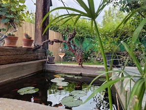 A garden with a pond, potted plants, and a glass of wine on a wooden ledge.