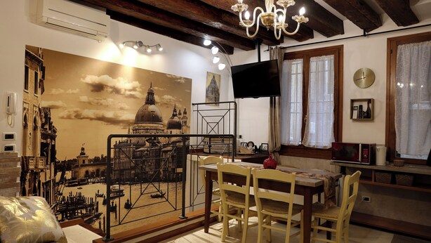 A dining area with a mural of a cityscape, a chandelier, a television, and a clock on the wall. - SUITE HAVEN IN VENICE WITH PRIVATE SPA (Venezia)