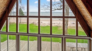 Vue depuis une chambre dotée de grandes fenêtres donnant sur une terrasse en bois et la plage.