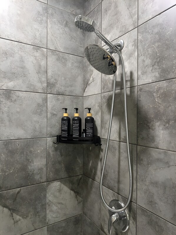A shower with a rain showerhead and a handheld showerhead, a shelf with three bottles of shampoo, conditioner, and body wash, and a handheld showerhead.