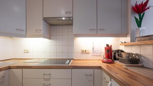 A modern kitchen with white cabinets, a wooden countertop, a red coffee machine, and a decorative red flower. - Studio in Duinbergen With Sea Views (Knokke-Heist)