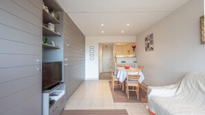 A modern living room with a flat-screen TV, a sofa, a dining table with chairs, and a kitchen in the background. - Studio in Duinbergen With Sea Views (Knokke-Heist)