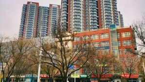 A high-rise building with multiple floors, surrounded by trees and various storefronts. - Elong ME Hotel (Shijiazhuang Railway Station Xinshizhong Road) (Shijiazhuang)