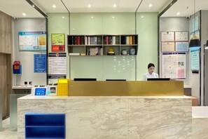 Un comptoir d’accueil avec un ordinateur, un présentoir d’information bleu et un mur avec des étagères remplies de livres et de certificats.