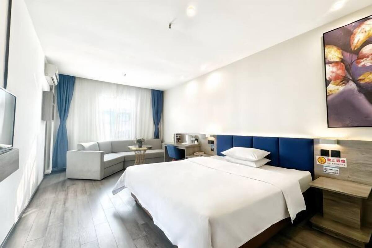 A modern hotel room with a large bed, a sofa, a desk, and a TV.