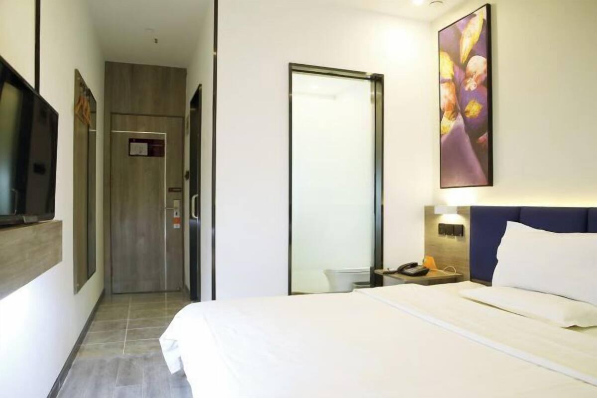 A hotel room with a bed, a nightstand, a wall-mounted TV, a door, and a painting.