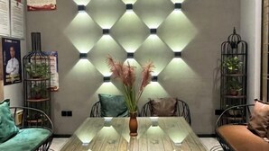 A dining area with a glass table, metal chairs, and a decorative wall with lights. - Elong ME Hotel (Shijiazhuang Railway Station Xinshizhong Road) (Shijiazhuang)