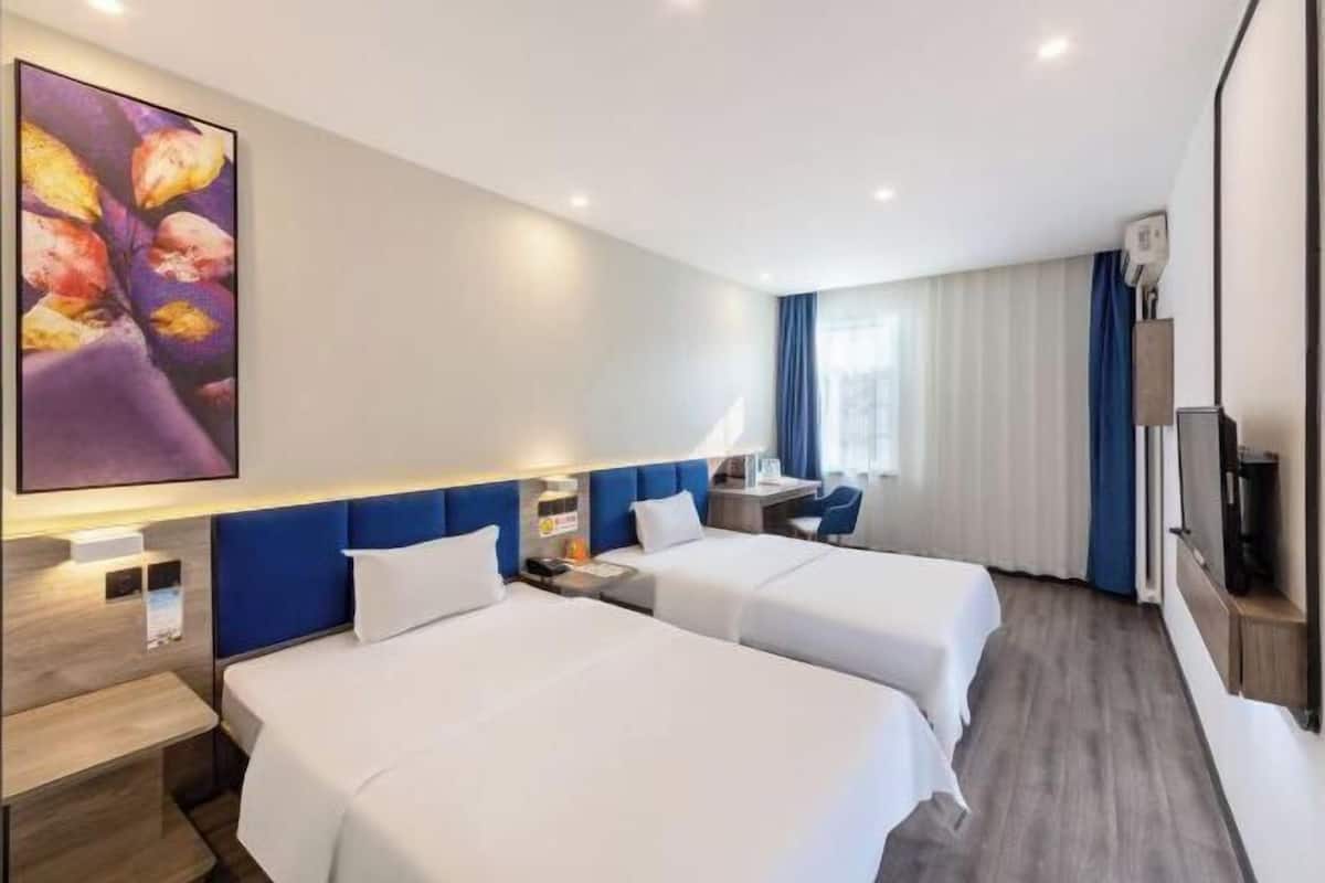 A hotel room with two beds, a desk, a chair, a TV, and a large painting on the wall.