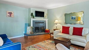 Ein Wohnzimmer mit Kamin, einem darüber montierten Fernseher, einem weißen Sofa mit roten Kissen und einem blauen Sessel.