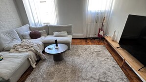 Un salon avec une moquette à poils longs de couleur grise, une table basse ronde, un canapé et un téléviseur posé sur un meuble en bois.