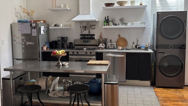 Une cuisine moderne équipée d’appareils électroménagers en acier inoxydable, un coin repas avec des tabourets et un lave-linge.