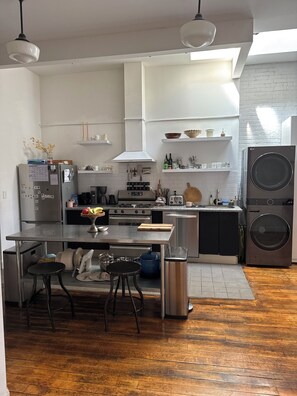 A modern kitchen with stainless steel appliances, a dining area with stools, and a laundry machine. - Spacious 3-bedroom apartment in terrific Williamsburg Brooklyn with AC, WiFi (Brooklyn)