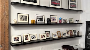 Une pièce avec des poutres en bois, une table noire et plusieurs étagères noires où sont exposées des photos encadrées et de petits objets décoratifs.