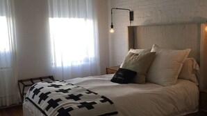 Une chambre à coucher avec un lit, un plancher en bois, des murs blancs et un mur d’accent en briques.