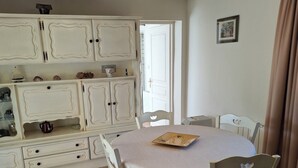 Un comedor con una mesa redonda, sillas blancas y un aparador con adornos.