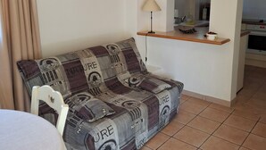 Una sala de estar con un sofá, una mesa, una lámpara y una cocina al fondo.