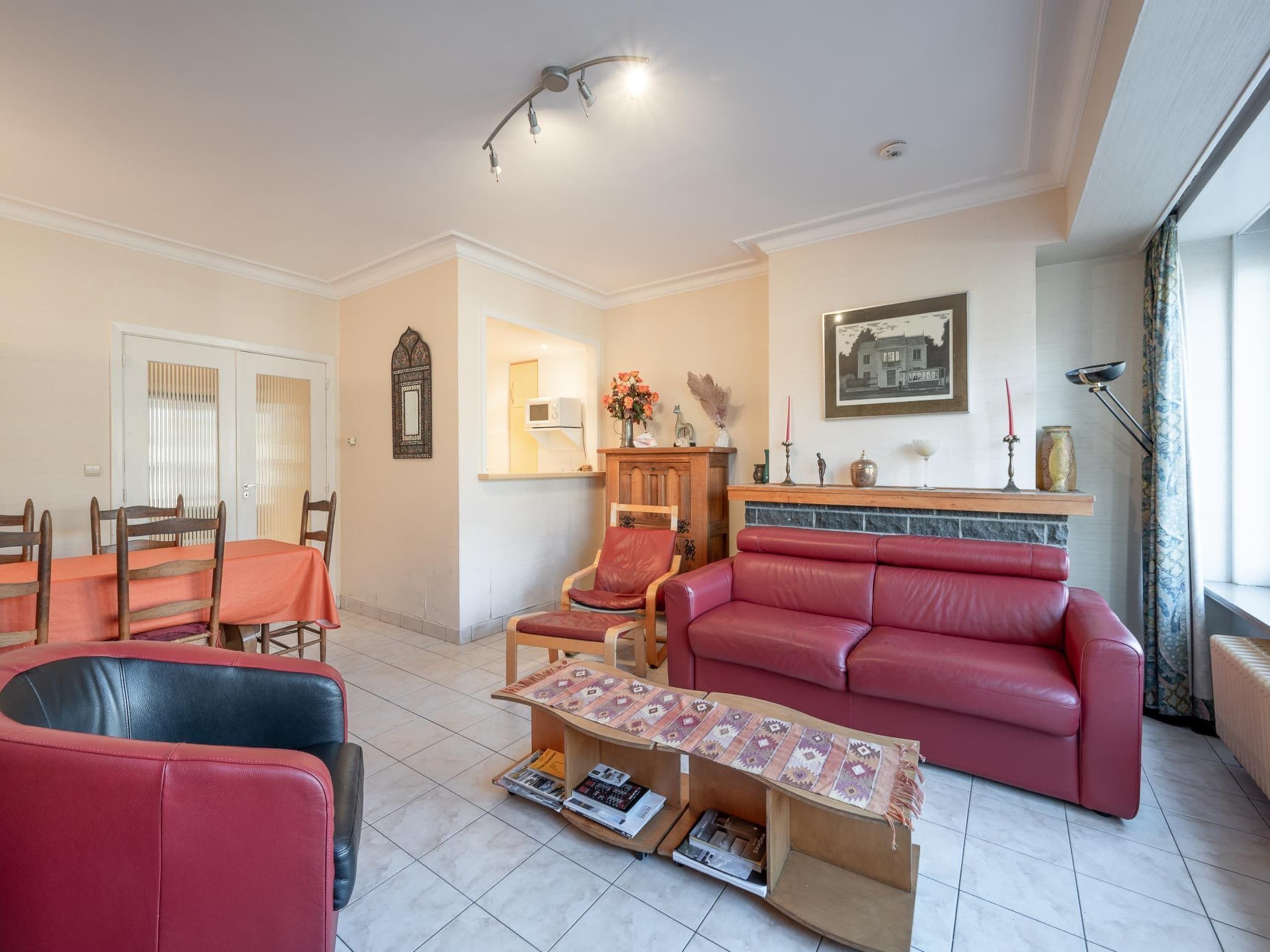 A living room with a red sofa, a wooden coffee table, a red armchair, and a dining area with a table and chairs.