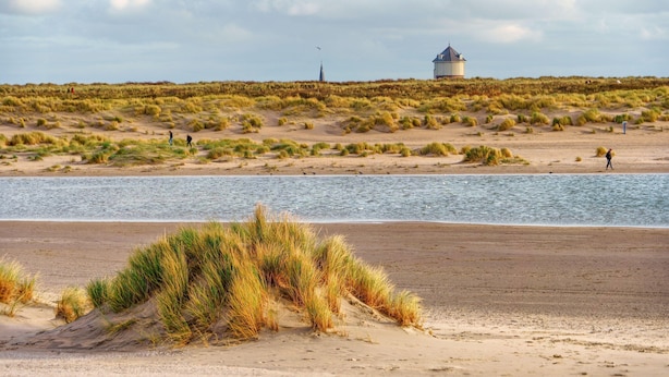 A coastal landscape with a sandy beach, grassy dunes, and a body of water. - Family Comfort Near Beach (Knokke-Heist)