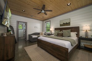 A bedroom with a wooden ceiling, a bed with a headboard, a nightstand, a lamp, a TV, and a window.