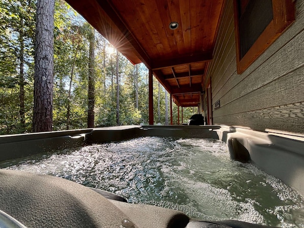 A hot tub in a forested area with a wooden ceiling and stone walls.