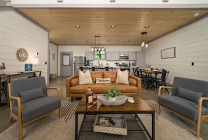 A modern living room with a brown leather sofa, two grey armchairs, a wooden coffee table, and a kitchen in the background.