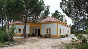 Un edificio amarillo y blanco con tejado de baldosas, rodeado de árboles y grava.