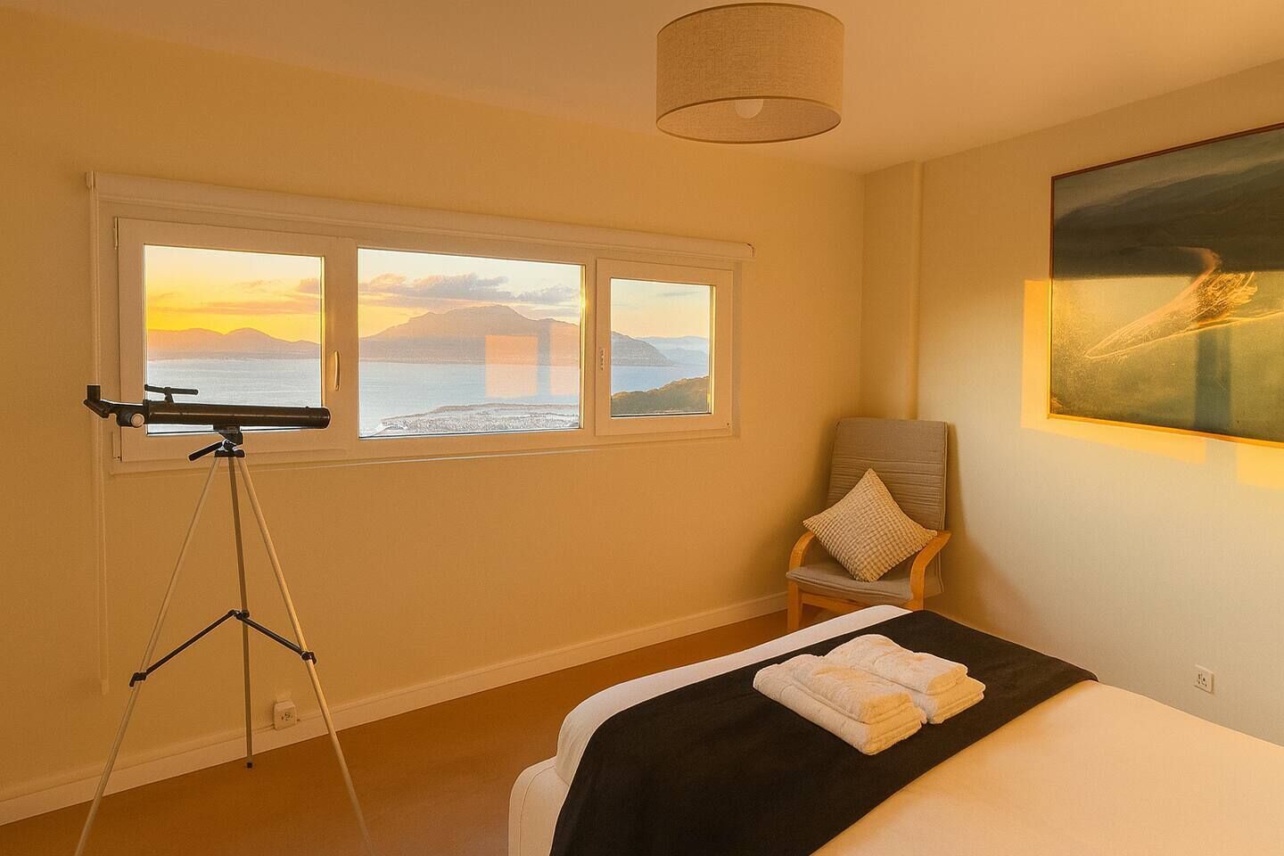 A room with a bed, a chair, a tripod, and a painting.