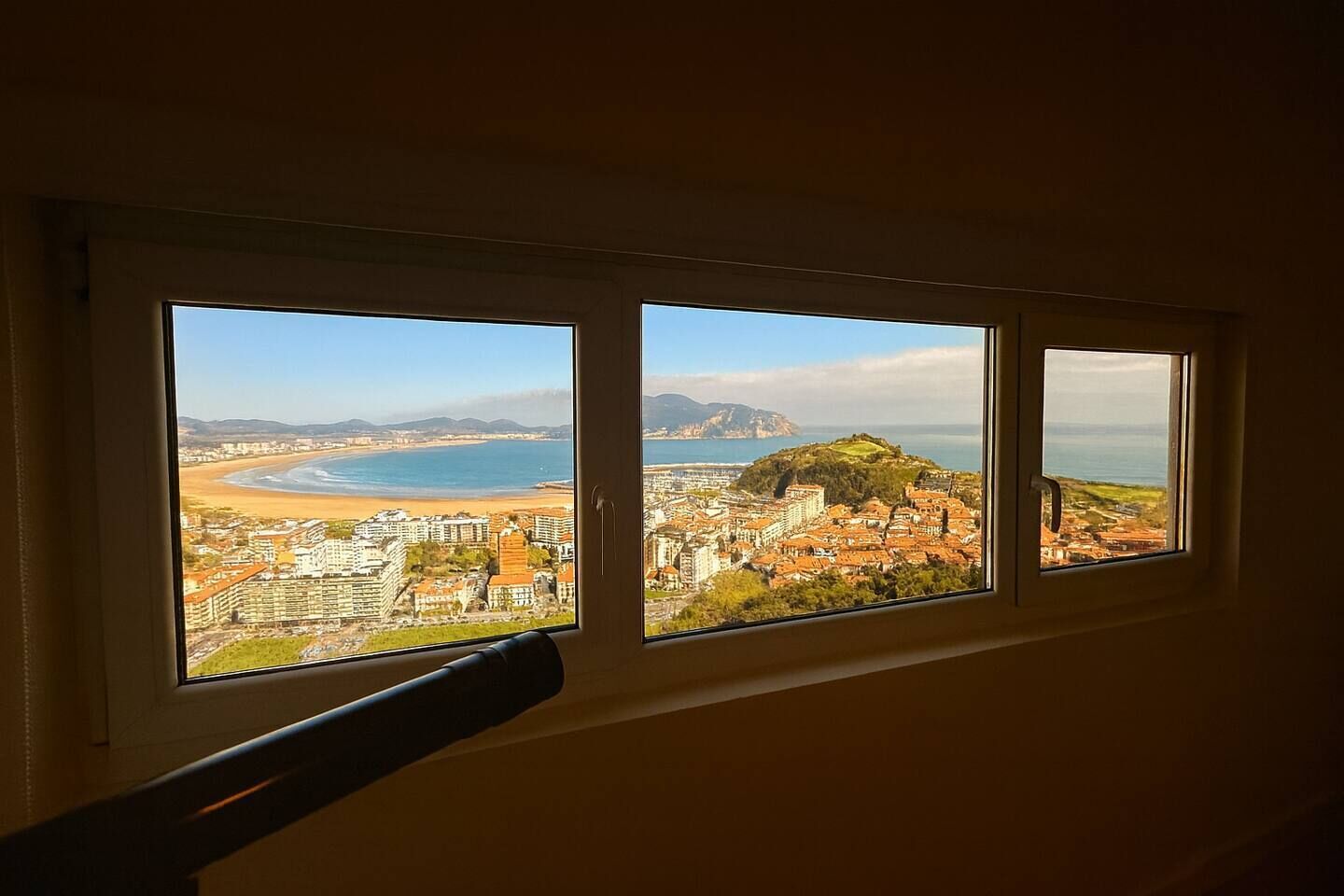 A window with a view of a coastal cityscape, including buildings and a beach.