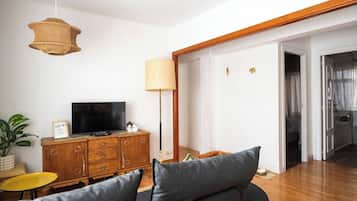 A living room with a sofa, a television on a wooden cabinet, a lamp, and a plant.