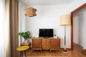 A room with a wooden cabinet, a television, a plant, a yellow stool, a hanging light fixture, and a floor lamp. - Casa Camilo - Retro con Encanto (Santander)