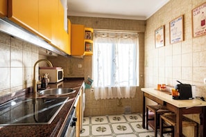 A kitchen with a sink, stove, microwave, and a window with curtains. There are signs on the wall indicating a coffee club and a wine club. - Casa Camilo - Retro con Encanto (Santander)