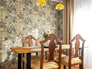 A dining area with a wooden table and chairs, a floral wallpaper, and yellow pendant lights. - Casa Camilo - Retro con Encanto (Santander)