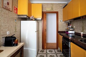 Una cocina pequeña con gabinetes amarillos, un refrigerador blanco y salpicadero de azulejos.