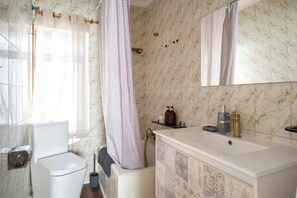 A bathroom with a white toilet, a bathtub, a sink with a gold faucet, and a mirror above the sink. - Casa Camilo - Retro con Encanto (Santander)